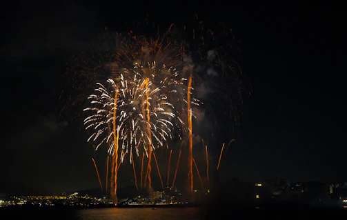 A vibrant burst of golden fireworks lighting up the night sky over a city skyline.