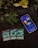 A smartphone displaying the Yu-Gi-Oh! Duel Links game title screen is placed on a dark surface surrounded by leaves and red berries. Below the phone, there are three Yu-Gi-Oh! trading cards laid out, depicting different characters.