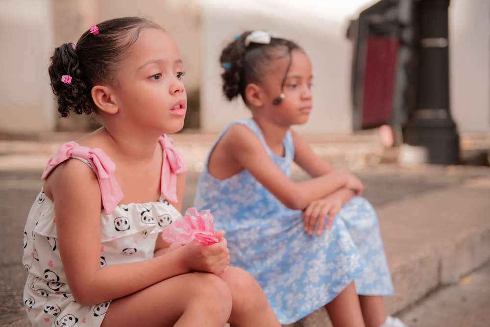 two little girls sitting on the side of the road