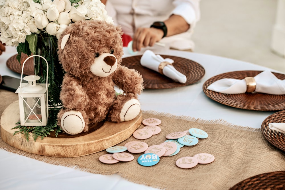 Un oso de peluche sentado en una mesa con un jarrón de flores