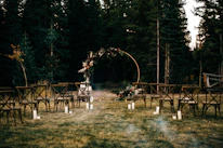A softly lit outdoor ceremony setup with white chairs and floral decorations on green grass.