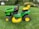 A bright green and yellow ride-on lawn mower sits on a well-manicured lawn, surrounded by lush greenery and trees in the background.