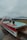 A unique hot tub designed in the shape of a boat, with two people relaxing inside. The setting appears to be by the seaside, with a misty and overcast sky in the background. The deck surrounding the hot tub is made of wooden planks.