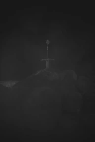 A close-up of a silver sword embedded in a stone circle surrounded by standing stones under a twilight sky.