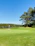A golfer teeing off on a lush green fairway under a clear blue sky at Pavenham Park Golf Club.
