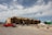 A large, multi-story building under construction with wooden framing visible. Several construction vehicles, including a red truck and a crane, are parked nearby. Piles of dirt and construction materials are scattered around the site under a partly cloudy sky.