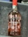 A bottle of Port Wine labeled 'DELAFORCE' with 'Rosé' below it is placed in a container filled with ice. The bottle has a red cap and is adorned with illustrations of various fruits such as cherries, watermelon slices, strawberries, oranges, and kiwis. There are visible liquid droplets on the bottle due to the cold ice.