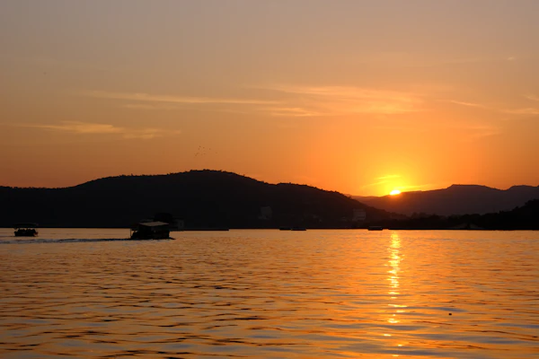 An orange sunset over Lake Pichola with boats on the water