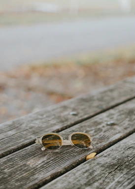 Close-up of trendy sunglasses resting on a sunlit wooden table with a beach background.
