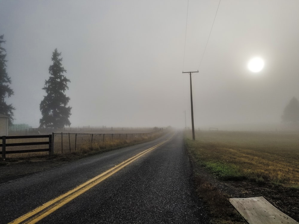 a foggy road with a fence and a light pole