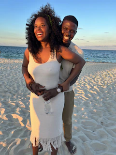 A happy couple stepping out of a Hamptons Ride taxi with the beach and blue sky in the background.