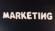 Wooden letters arranged to spell the word 'MARKETING' on a black textured background.