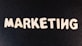 Wooden letters arranged to spell the word 'MARKETING' on a black textured background.