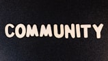 The word 'COMMUNITY' is spelled out with white wooden letters on a dark black background.