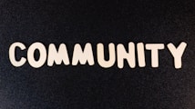 The word 'COMMUNITY' is spelled out with white wooden letters on a dark black background.