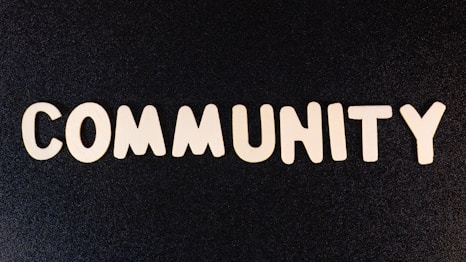 The word 'COMMUNITY' is spelled out with white wooden letters on a dark black background.