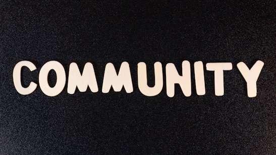 The word 'COMMUNITY' is spelled out with white wooden letters on a dark black background.