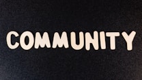 The word 'COMMUNITY' is spelled out with white wooden letters on a dark black background.