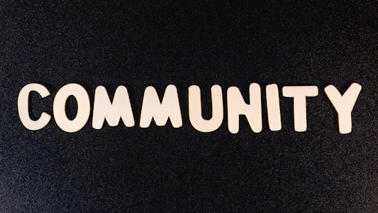 The word 'COMMUNITY' is spelled out with white wooden letters on a dark black background.