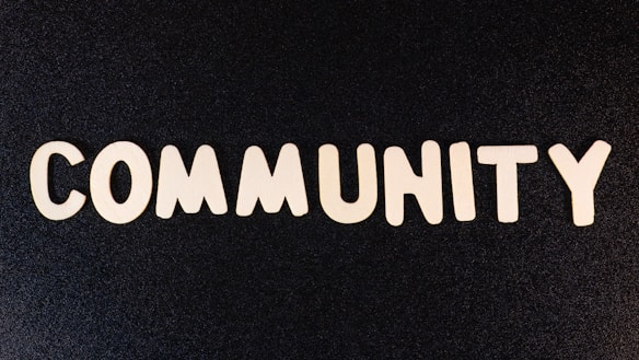 The word 'COMMUNITY' is spelled out with white wooden letters on a dark black background.
