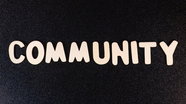 The word 'COMMUNITY' is spelled out with white wooden letters on a dark black background.