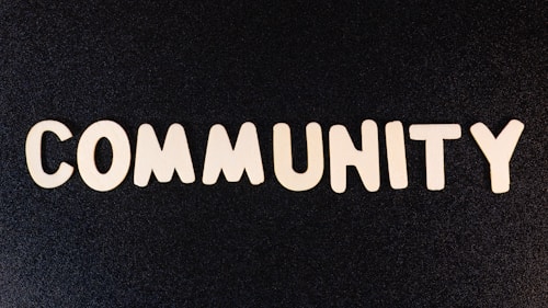 The word 'COMMUNITY' is spelled out with white wooden letters on a dark black background.