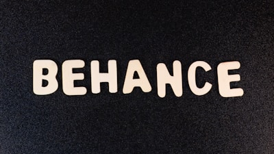 Block letters spelling 'BEHANCE' are arranged on a dark background, appearing in a casual, playful font.