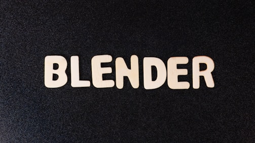 Wooden letters spell out the word 'BLENDER' against a black textured background. The letters have a natural wooden finish, creating a strong contrast with the dark surface.