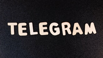 Wooden letters spelling out the word 'TELEGRAM' are arranged on a dark, textured surface.