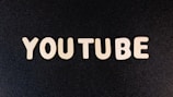 The word 'YOUTUBE' is displayed in white, bold, block letters against a black textured background.