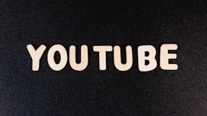The word 'YOUTUBE' is displayed in white, bold, block letters against a black textured background.