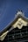 A section of a traditional Japanese roof with ornate designs, featuring intricate gold patterns and embellishments against a deep blue sky. The roof showcases detailed craftsmanship with coiled tiles and decorative gold elements.