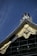 A section of a traditional Japanese roof with ornate designs, featuring intricate gold patterns and embellishments against a deep blue sky. The roof showcases detailed craftsmanship with coiled tiles and decorative gold elements.