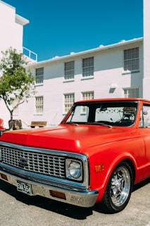 A shiny red pickup truck parked in front of the Winnipeg West Automotive Group dealership under a clear blue sky.