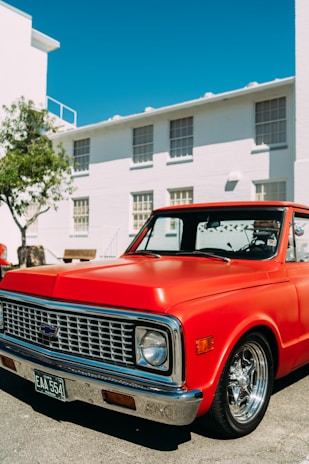 A shiny red pickup truck parked in front of the Winnipeg West Automotive Group dealership under a clear blue sky.