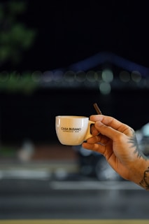 Artistic shot of a tattooed hand holding a coffee cup, highlighting the waterproof inknoir design in daylight