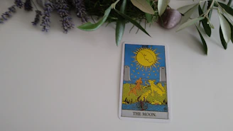 A close-up of the Moon tarot card featuring a luminous full moon over a mysterious landscape with two towers.