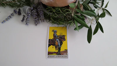 A detailed illustration of the Page of Pentacles tarot card, glowing softly against a dark, mystical background.
