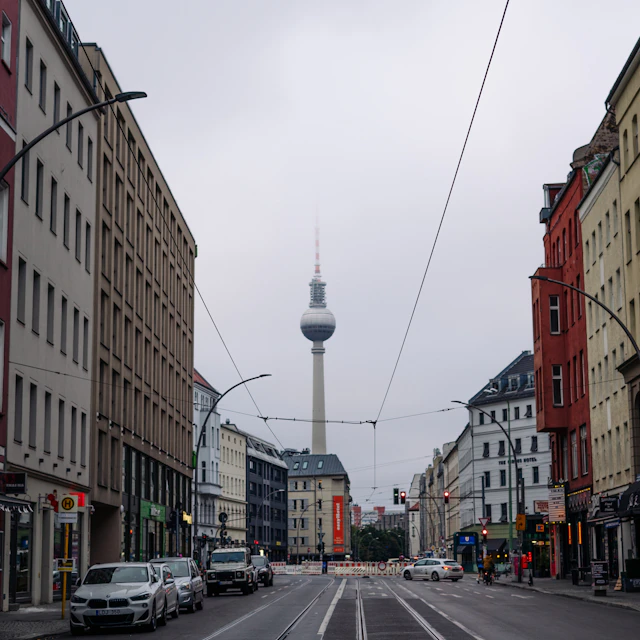 A grey morning street in Berlin with a car, a traffic light and the TV tower in the distance