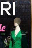 Flowing midi dress in deep emerald green displayed on a mannequin near a sunlit window.