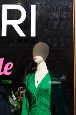 Flowing midi dress in deep emerald green displayed on a mannequin near a sunlit window.