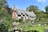 A charming thatched cottage with half-timbered walls is surrounded by lush greenery and a well-tended garden. Several people are engaged in gardening activities, hinting at a lively and productive atmosphere.