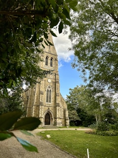A warm, inviting photo of the church entrance with sunlight filtering through nearby trees.