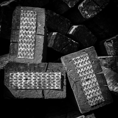 Several wooden blocks display metal plates with evenly spaced perforations, creating a textured surface. The image is rendered in black and white, emphasizing the contrast and details of the wood grain and metal.