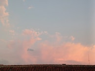 A tile roof is silhouetted against a sky filled with soft pink and blue clouds. The sky is light and calm, suggesting a time around sunset or sunrise. An antenna is visible on the right side, slightly above the roofline.