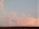 A tile roof is silhouetted against a sky filled with soft pink and blue clouds. The sky is light and calm, suggesting a time around sunset or sunrise. An antenna is visible on the right side, slightly above the roofline.