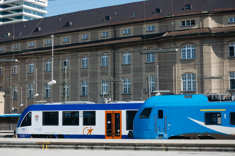 a blue and white train traveling past a tall building