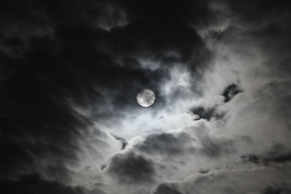 a full moon in a cloudy sky with dark clouds