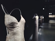 A close-up view of an elegant dress with shimmering sequins and a textured pattern. The dress has thin straps and a deep neckline, showcasing intricate details in design. It is set against a dark, blurred background.