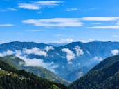 Majestic mountains covered in lush green forest with a clear blue sky.